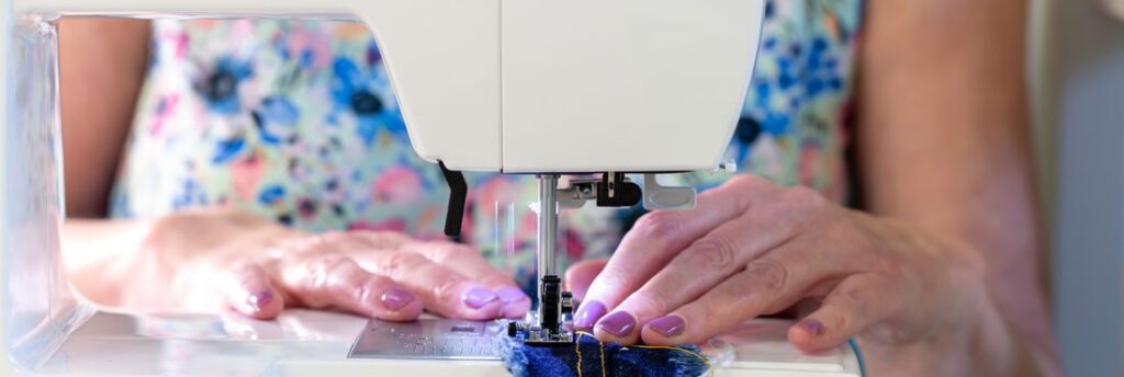 image is a close up of a modern, white sewing machine with two white female hands feeding material under the needle.